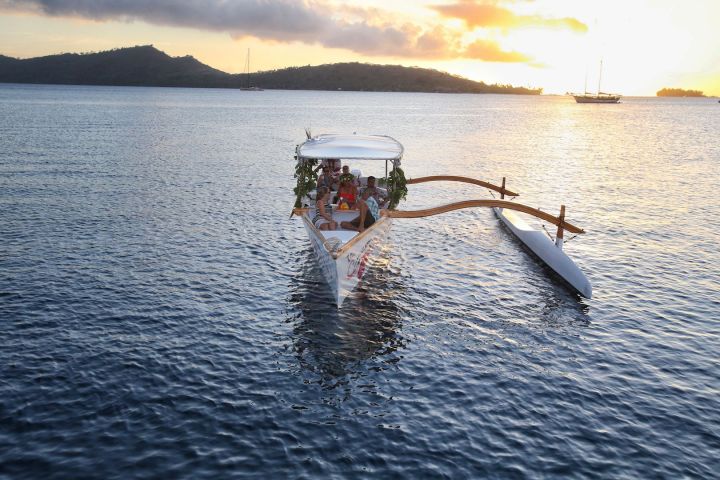 An outrigger canoe sailing in Bora Bora at sunset time