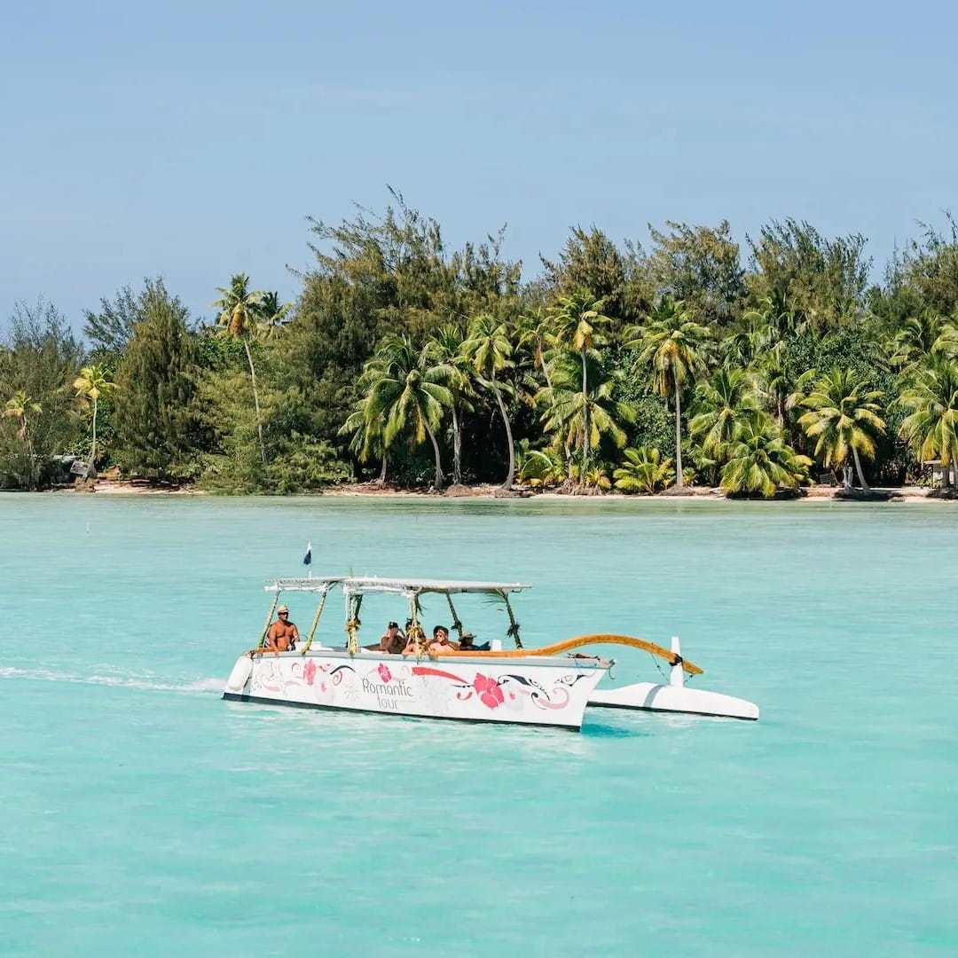Boat on turquoise water near tropical island with palm trees.